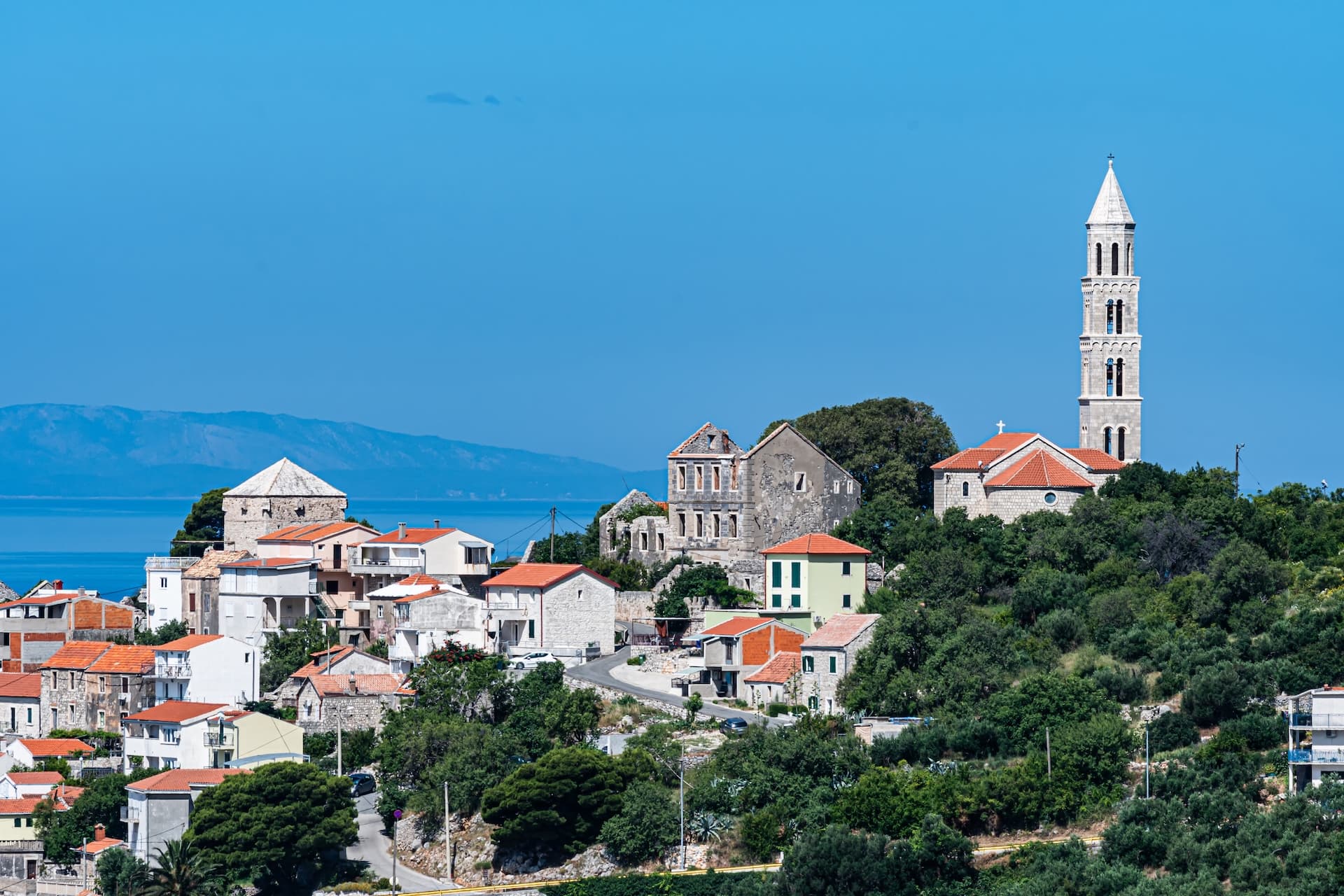 Drvenik village with stone church bell tower overlooking the blue sea and distant mountains.