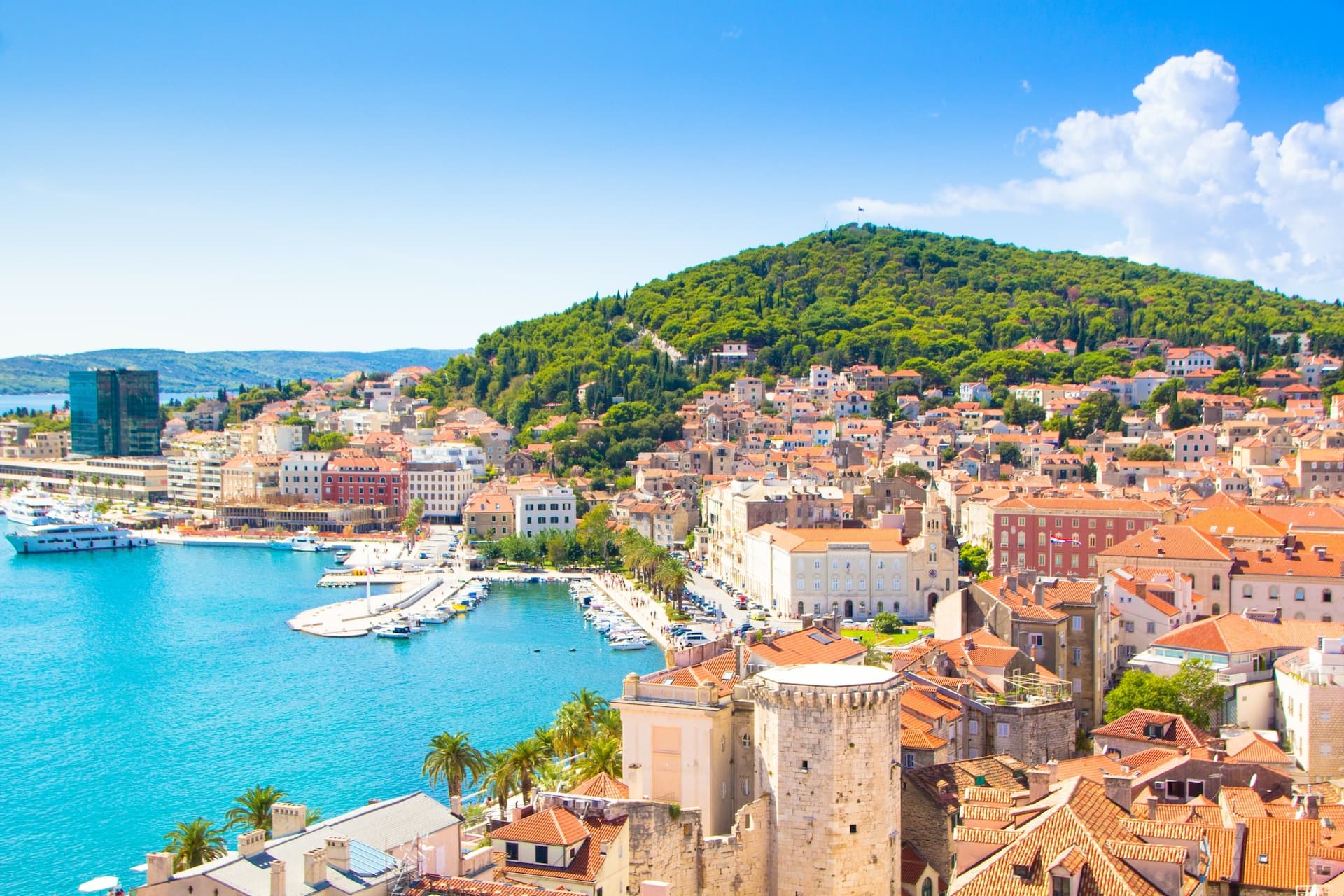 Coastal city view with terracotta roofs, turquoise harbor, and lush green Marjan Hill.