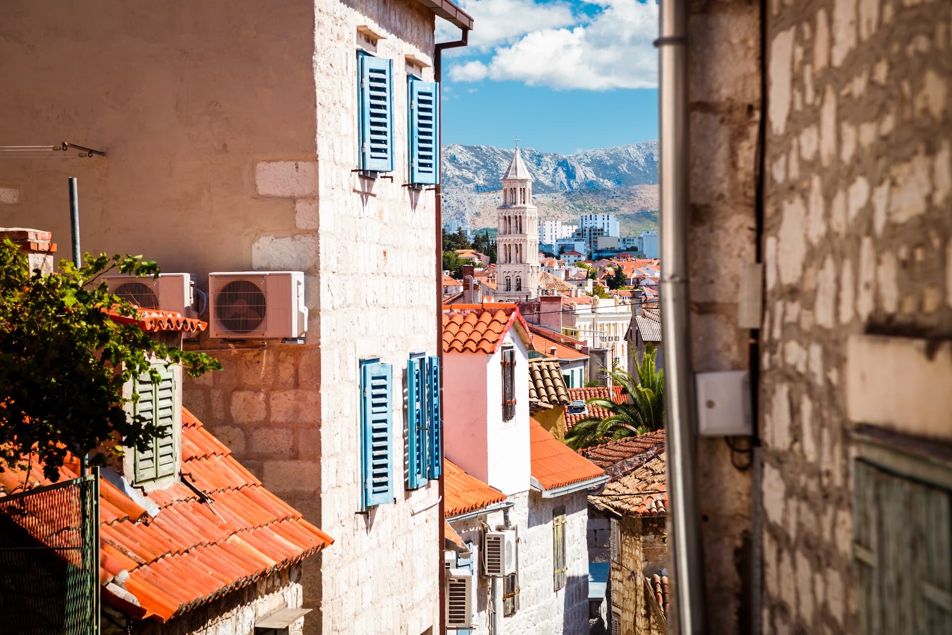 Narrow street view of Split rooftops, bell tower, and mountains under a blue sky.