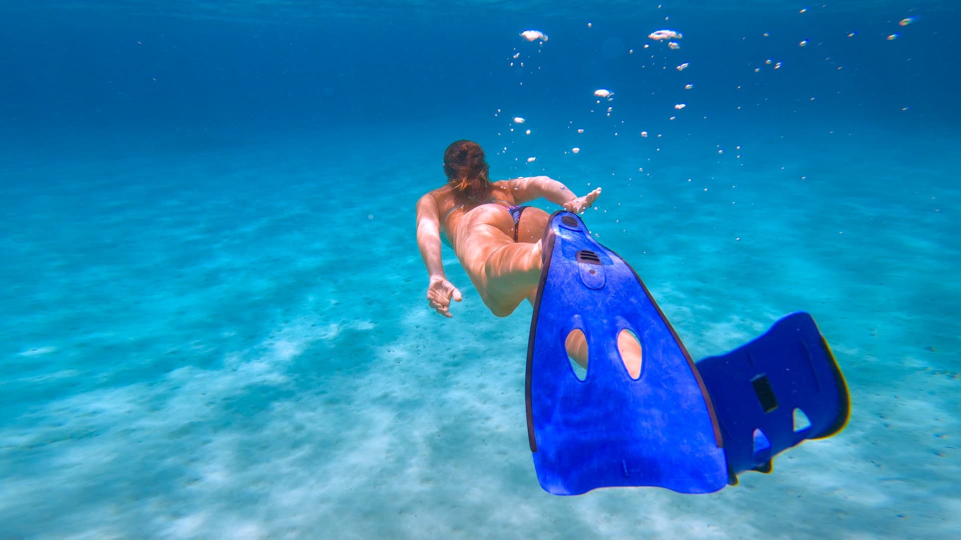 Snorkeler with blue fins swimming above sandy bottom in clear turquoise water at Pakleni Islands.