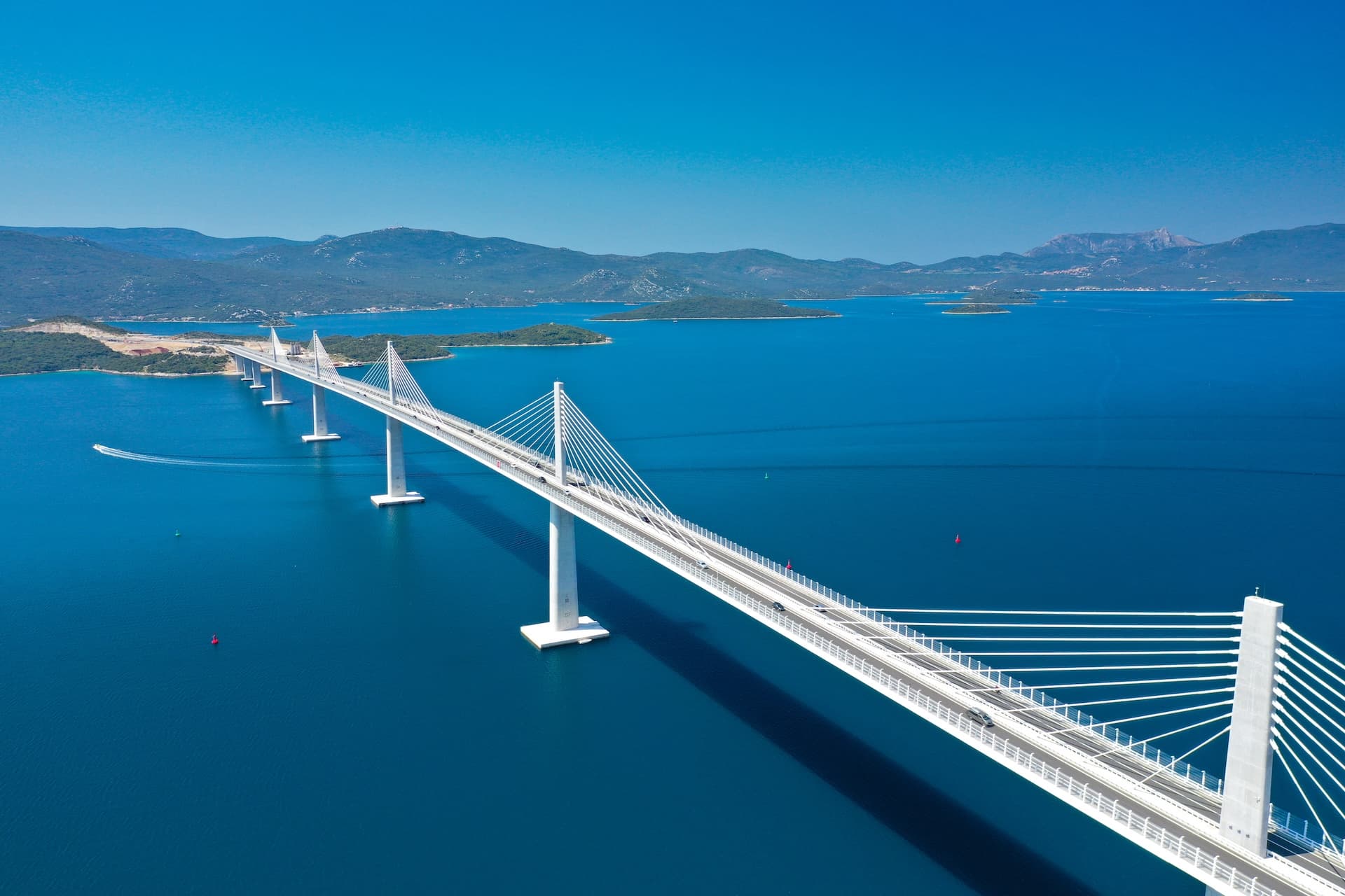 Cable-stayed bridge over deep blue sea with distant green islands and mountains, Pelješac.
