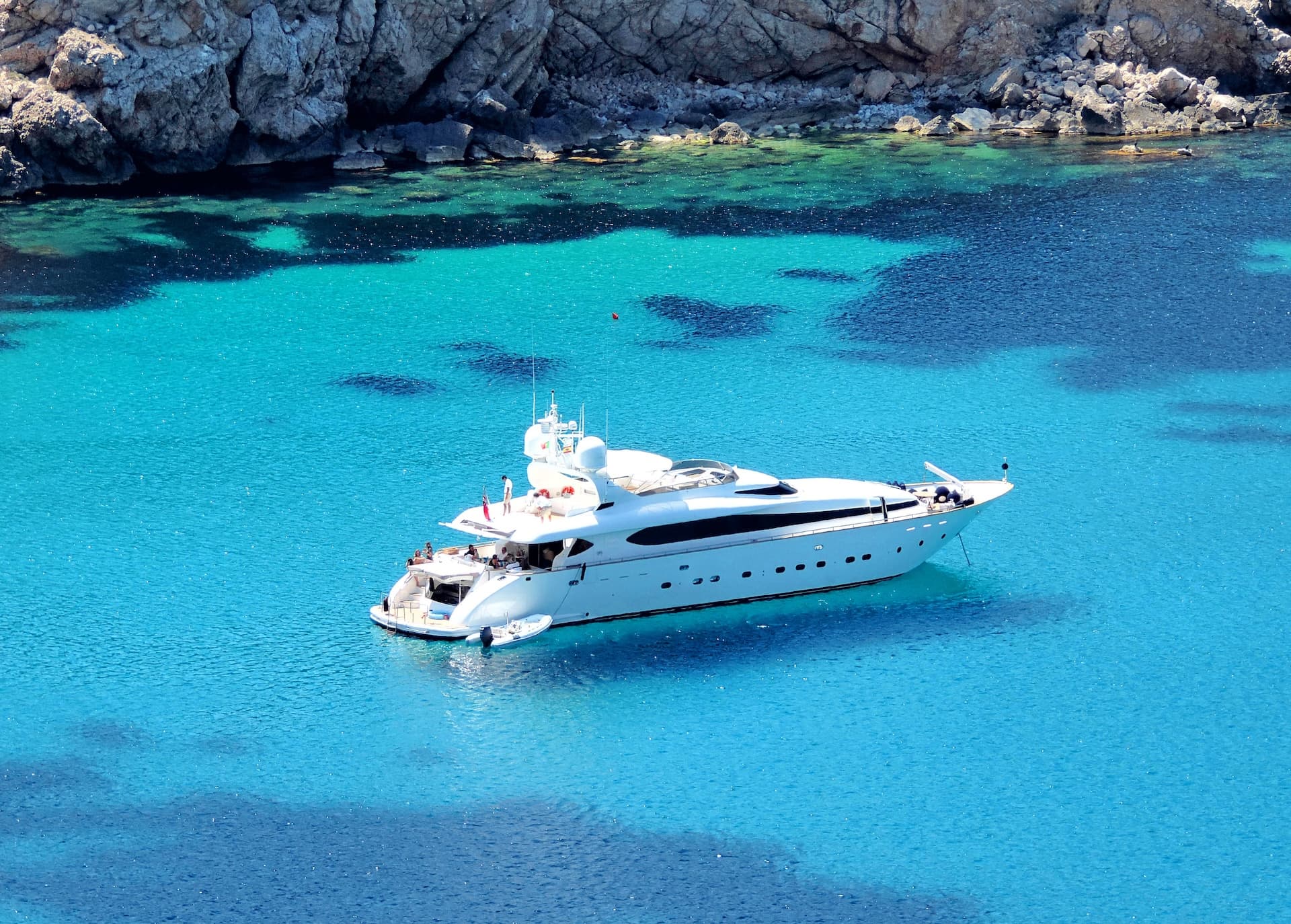 White yacht anchored in clear turquoise coastal waters near rocky shore