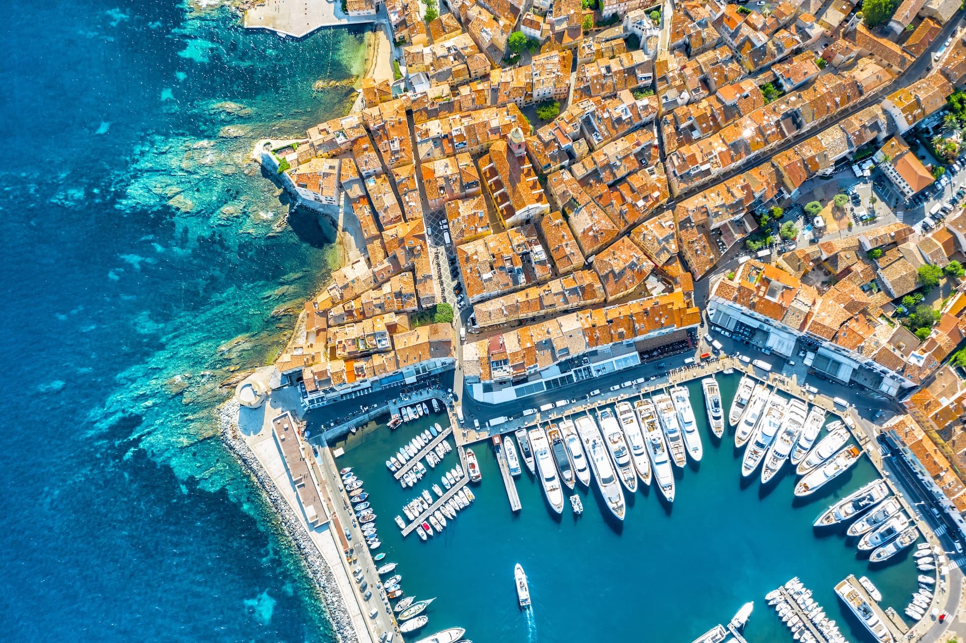 Aerial view of Dubrovnik marina with many yachts docked next to historic orange-roofed buildings.