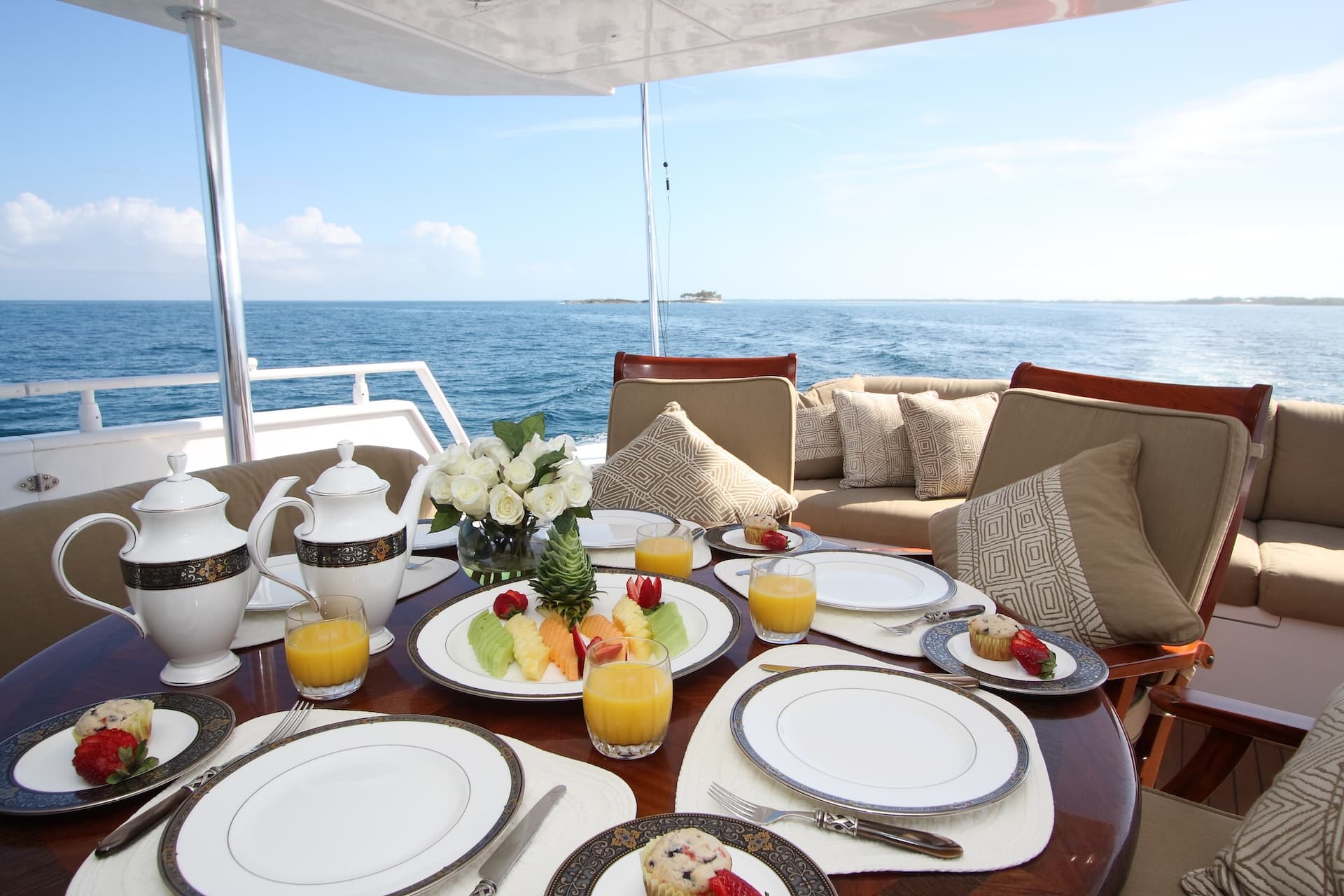 Breakfast served on a yacht deck with fruit, juice, and pastries overlooking the blue sea.