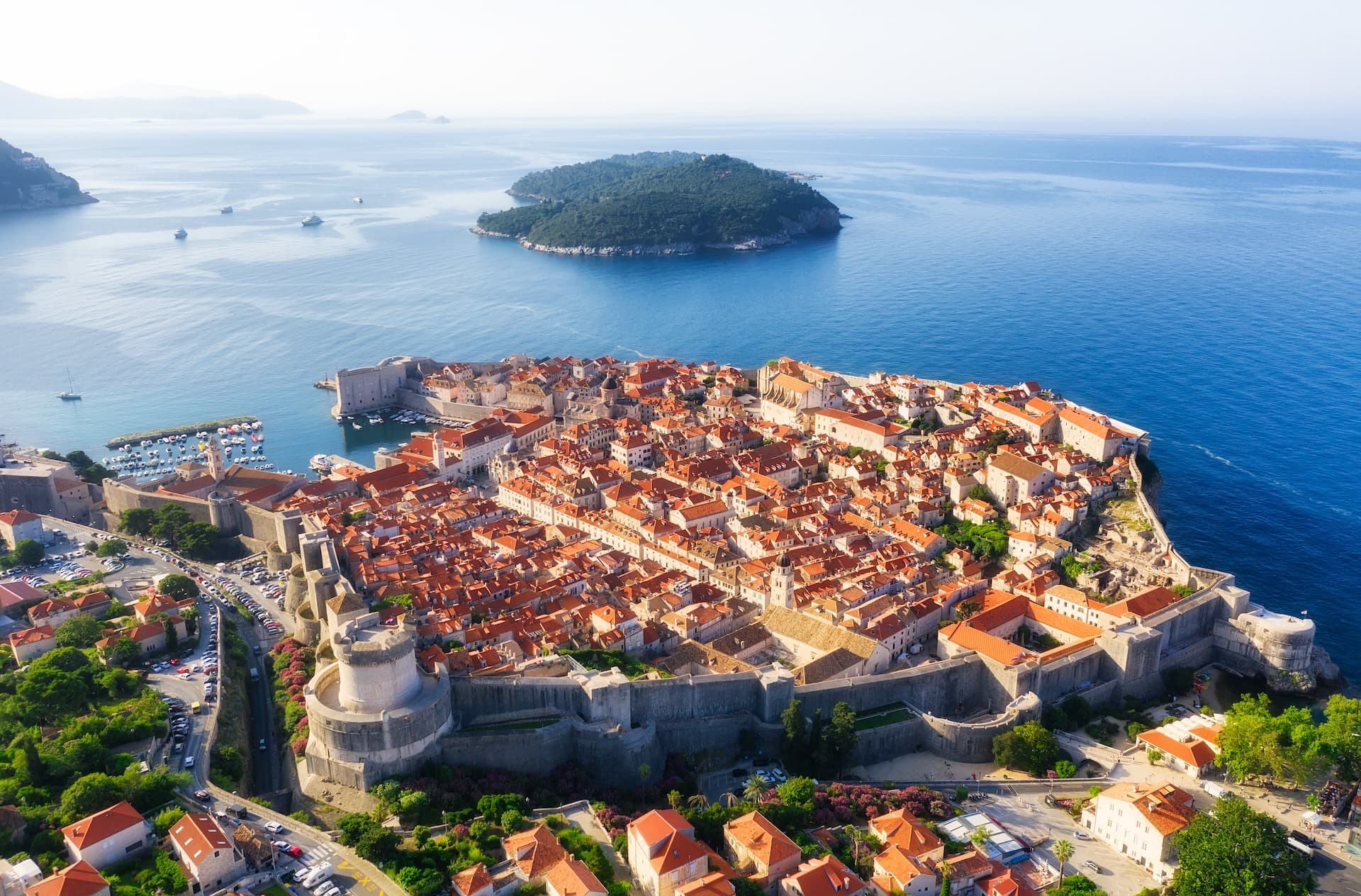 Aerial view of Dubrovnik Old Town walls, terracotta roofs, and blue Adriatic Sea with Lokrum Island.