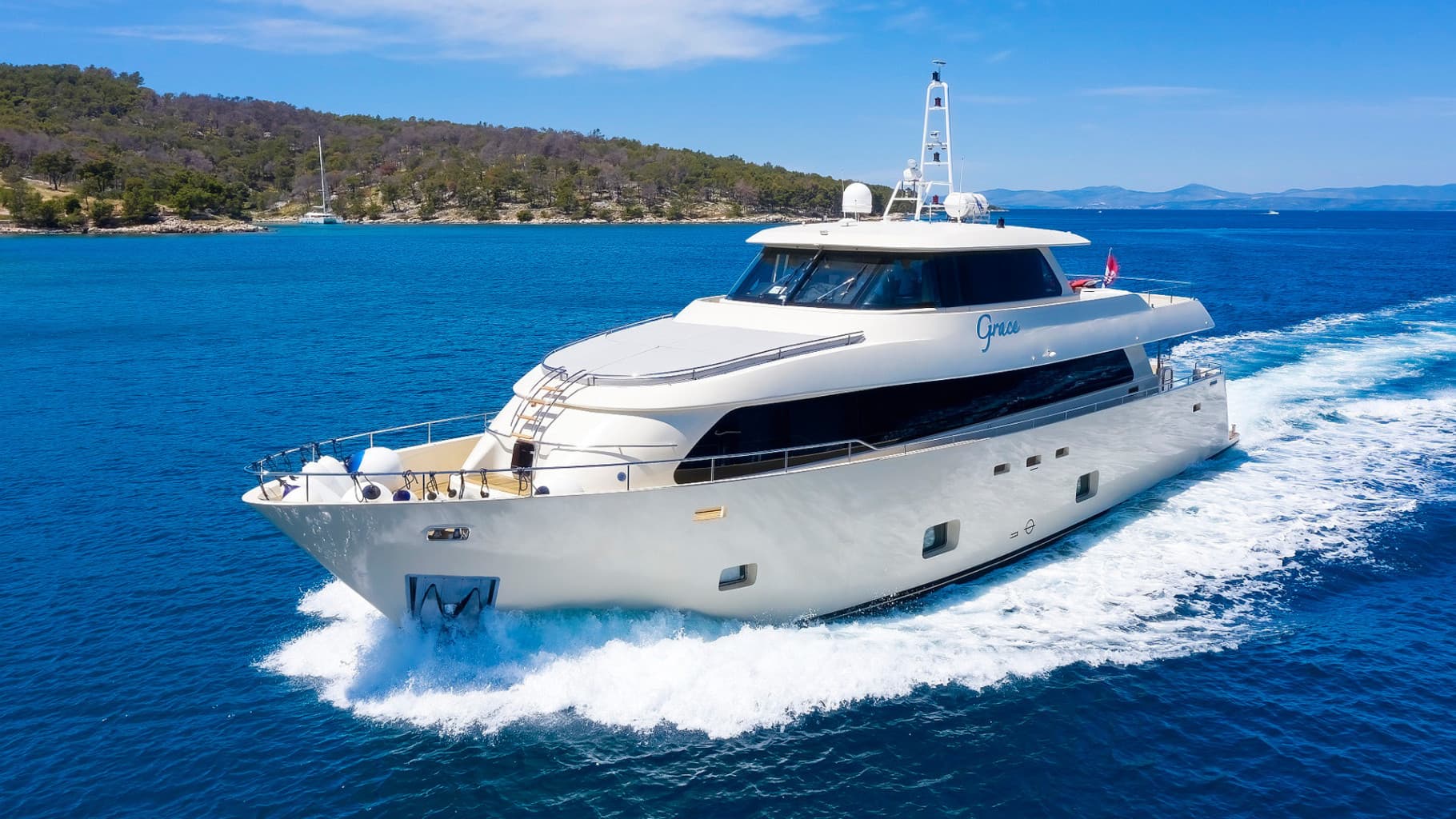 White motor yacht named Grace speeding through deep blue coastal waters near a wooded island.