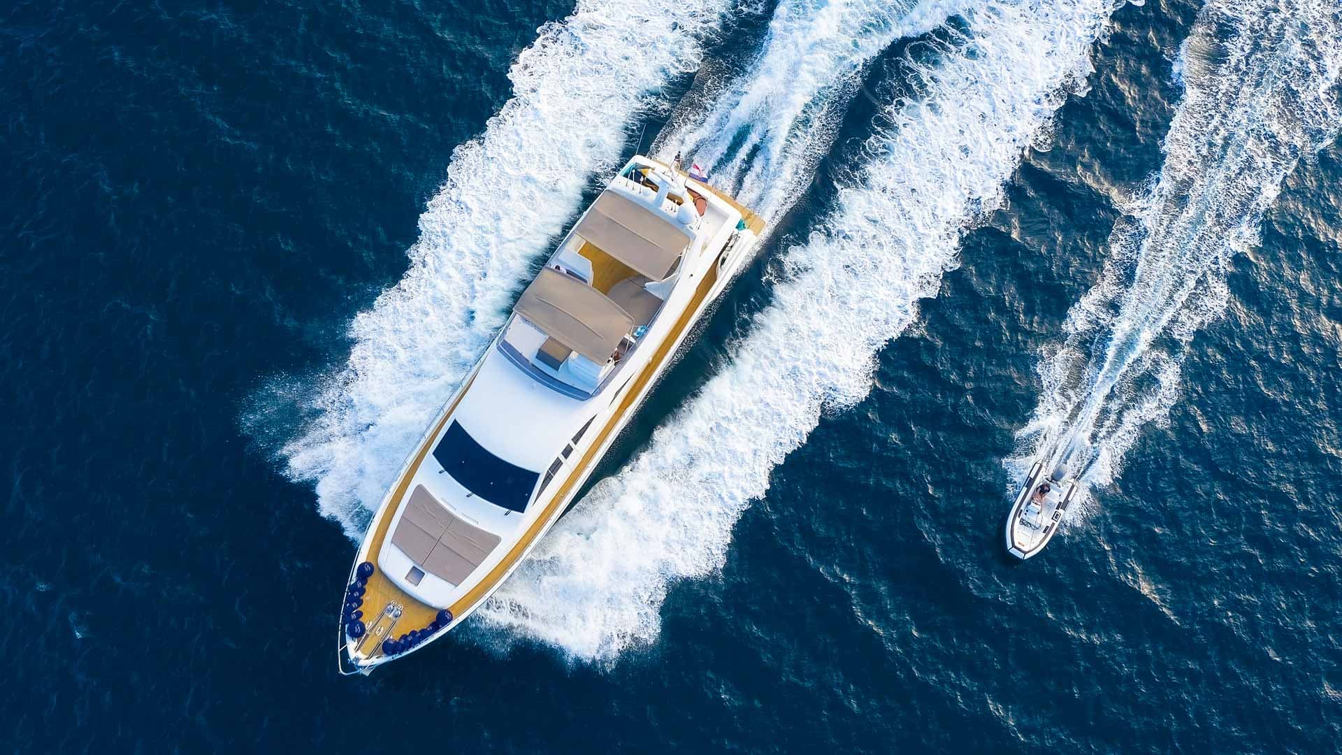 Luxury yacht and small boat speeding across deep blue ocean water, creating white wakes.