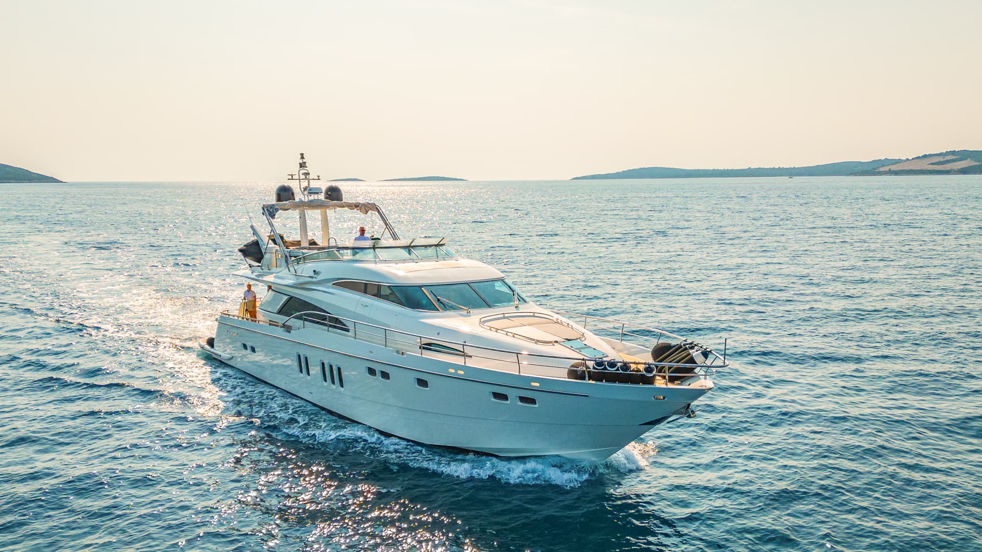 Motor yacht cruising on blue sea water near hilly coastline at sunset