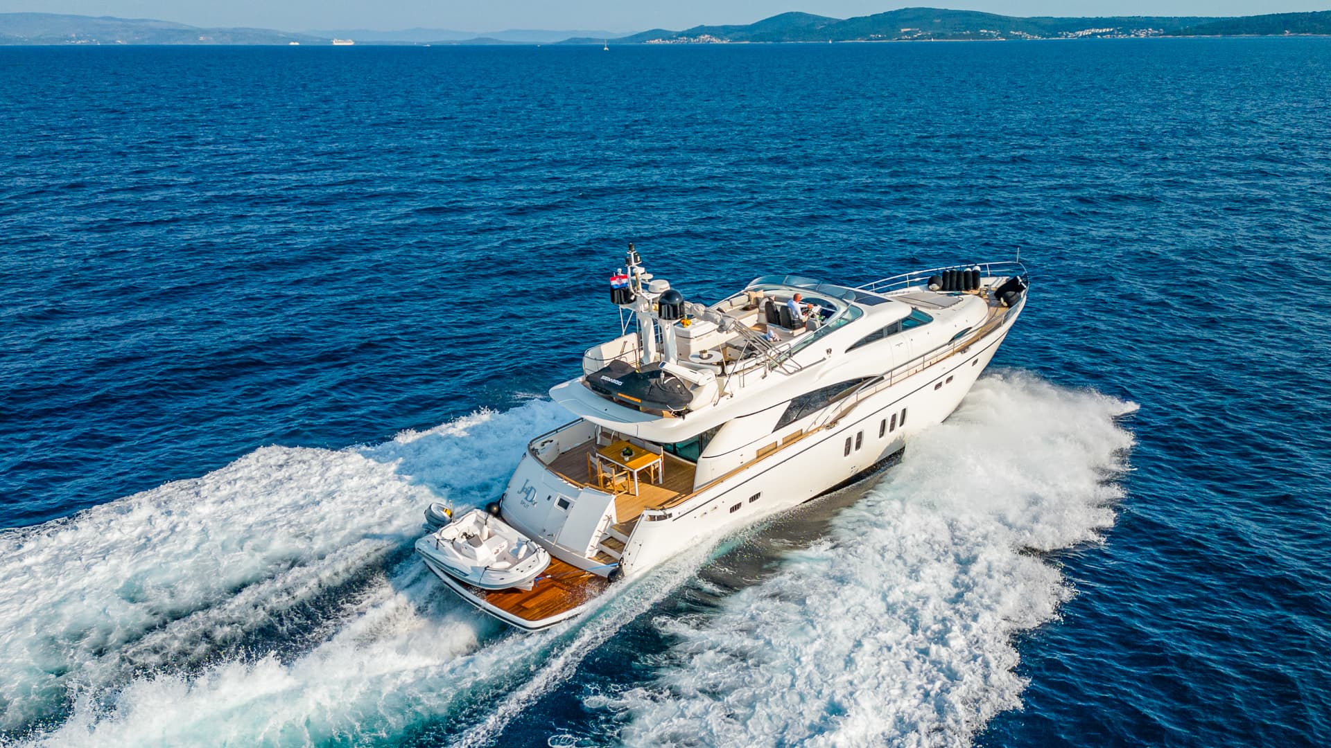 White motor yacht speeding through deep blue sea with distant coastline visible