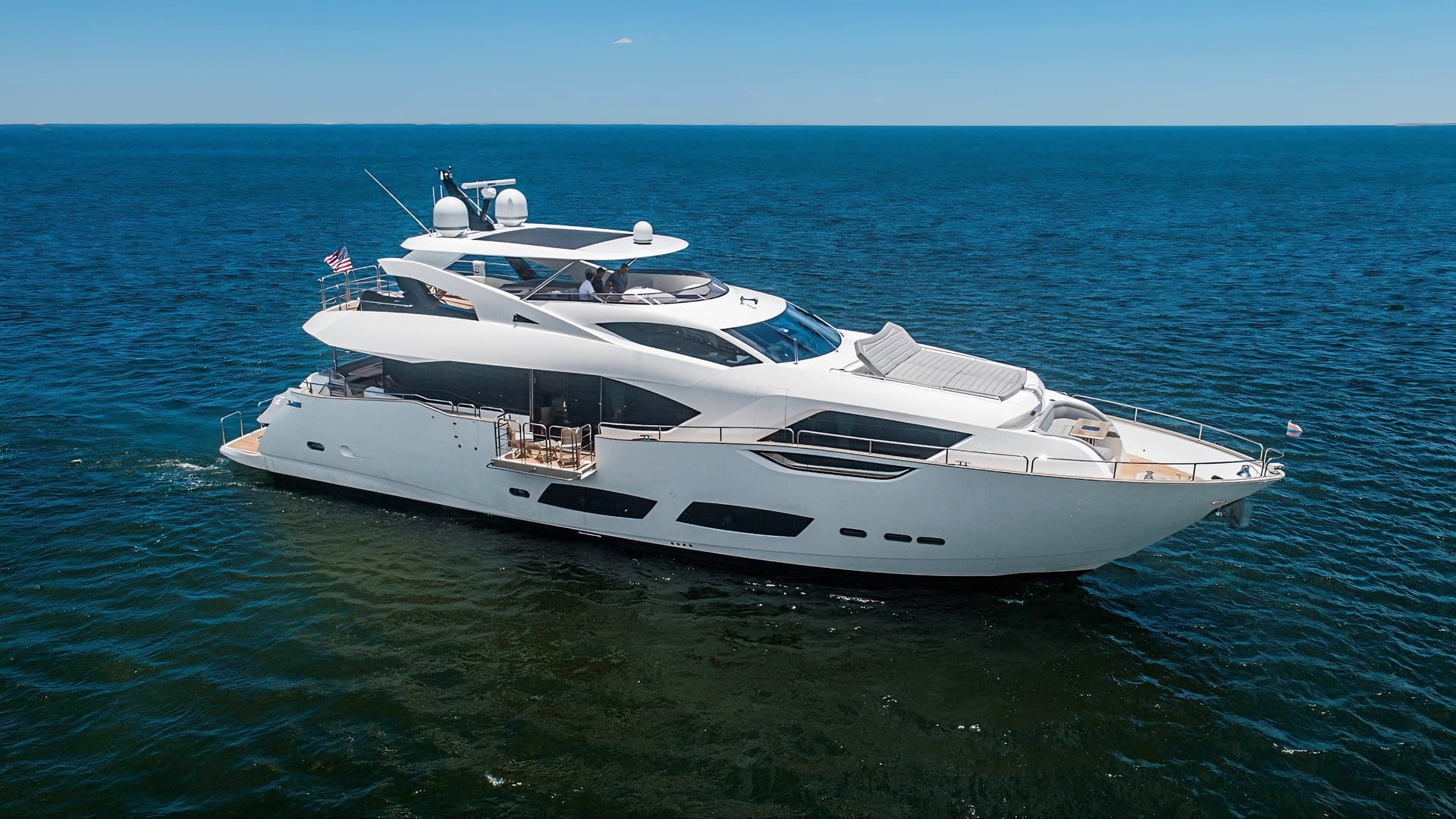 Large white motor yacht cruising on dark blue water under a clear blue sky