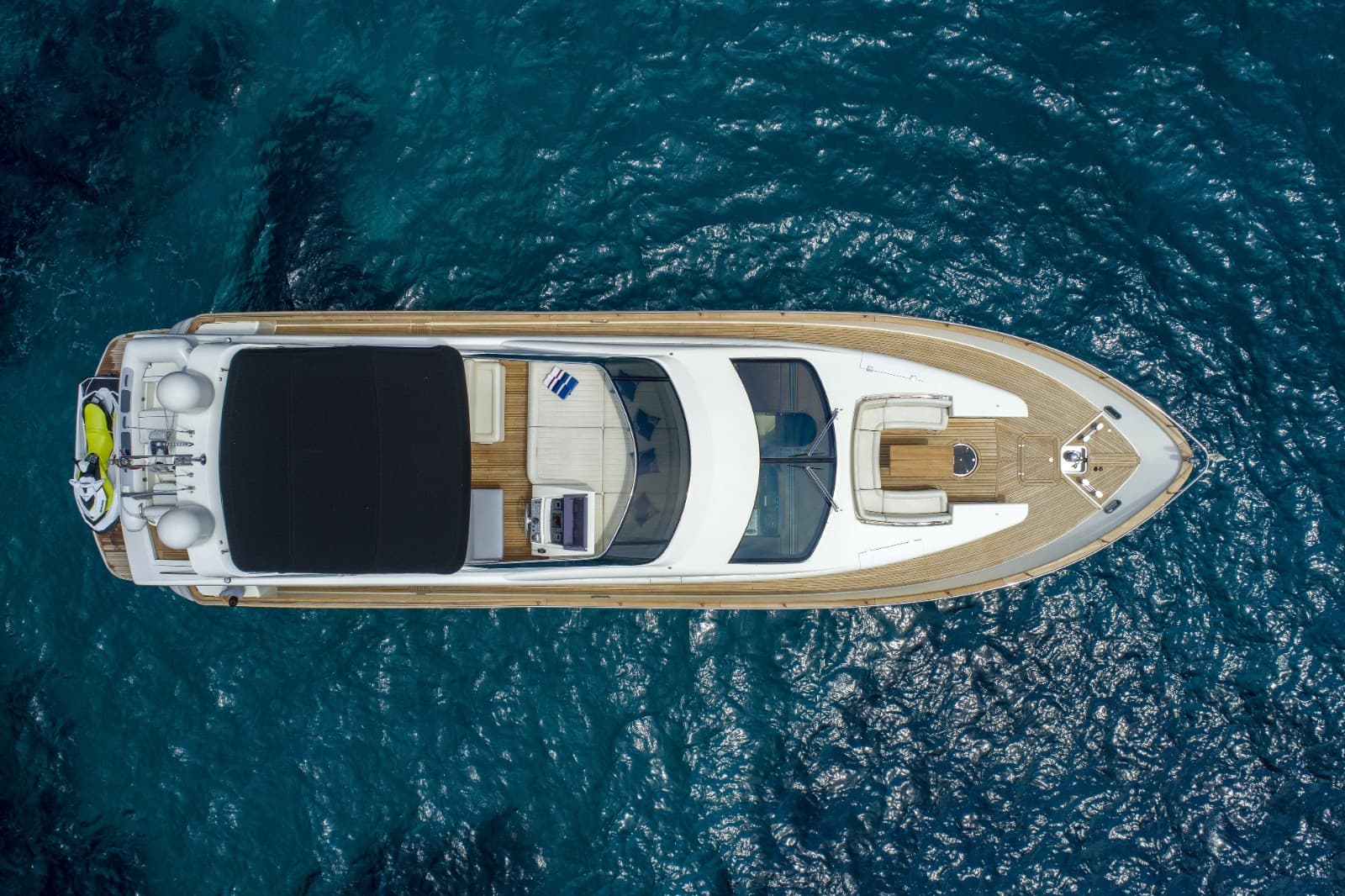 Aerial view of white motor yacht with teak deck on deep blue, rippling sea water.