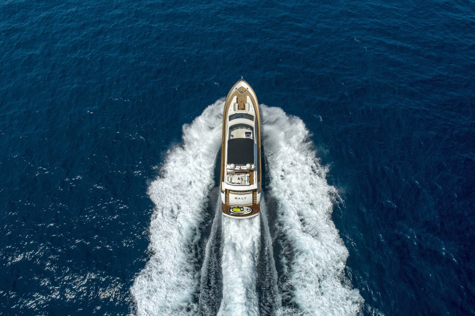 Motor yacht named SALT speeding across deep blue ocean water leaving a white wake.
