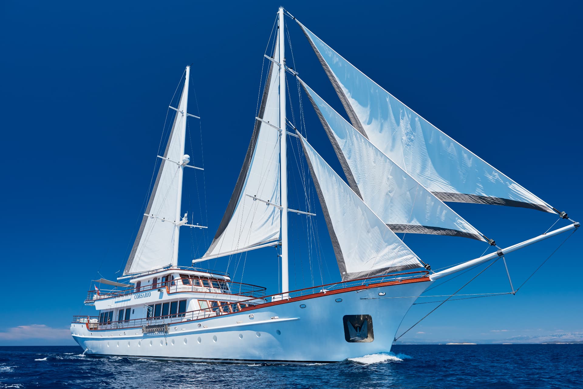White sailing yacht named Corsario cruising on deep blue sea under clear sky