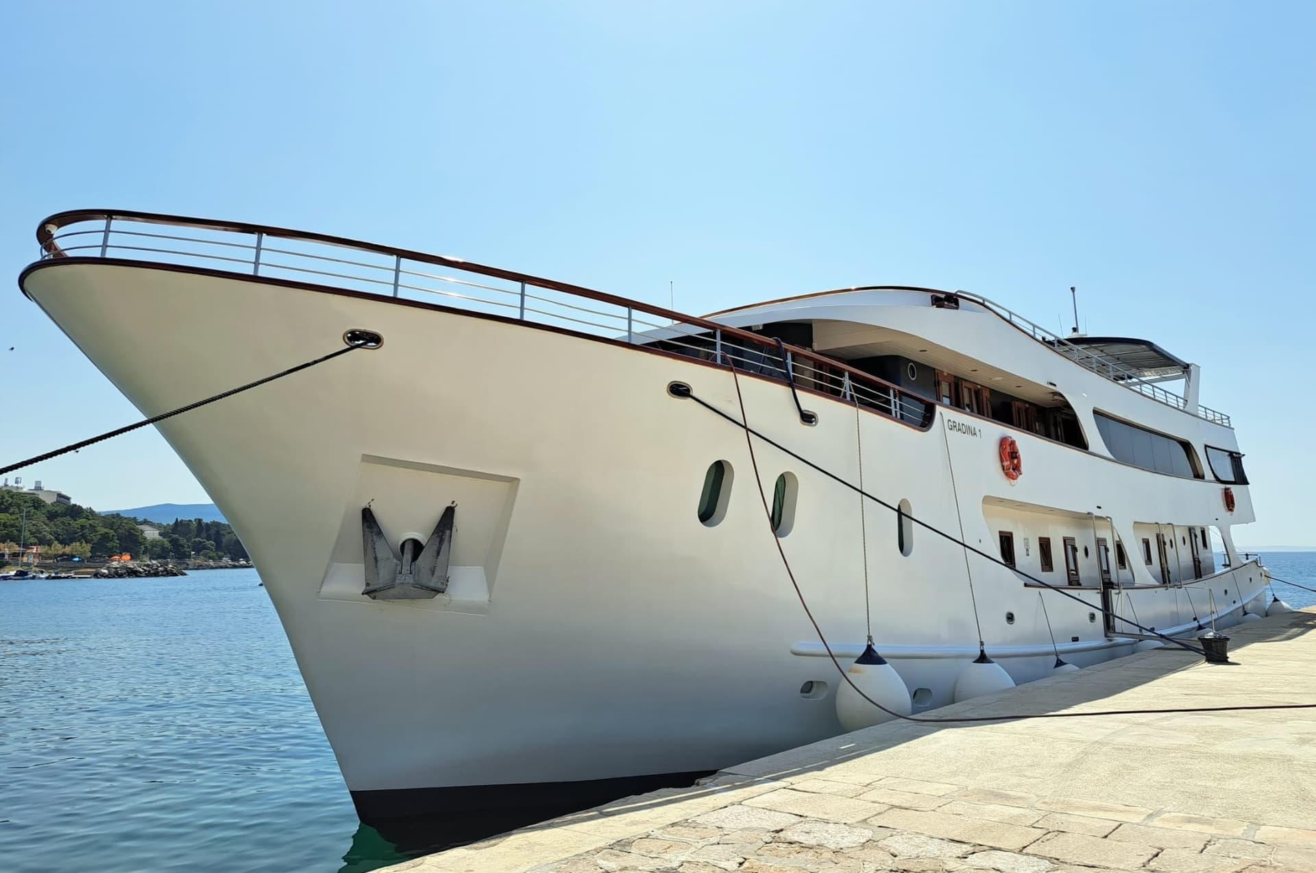 White yacht named GRADINA 1 docked at stone pier under clear blue sky
