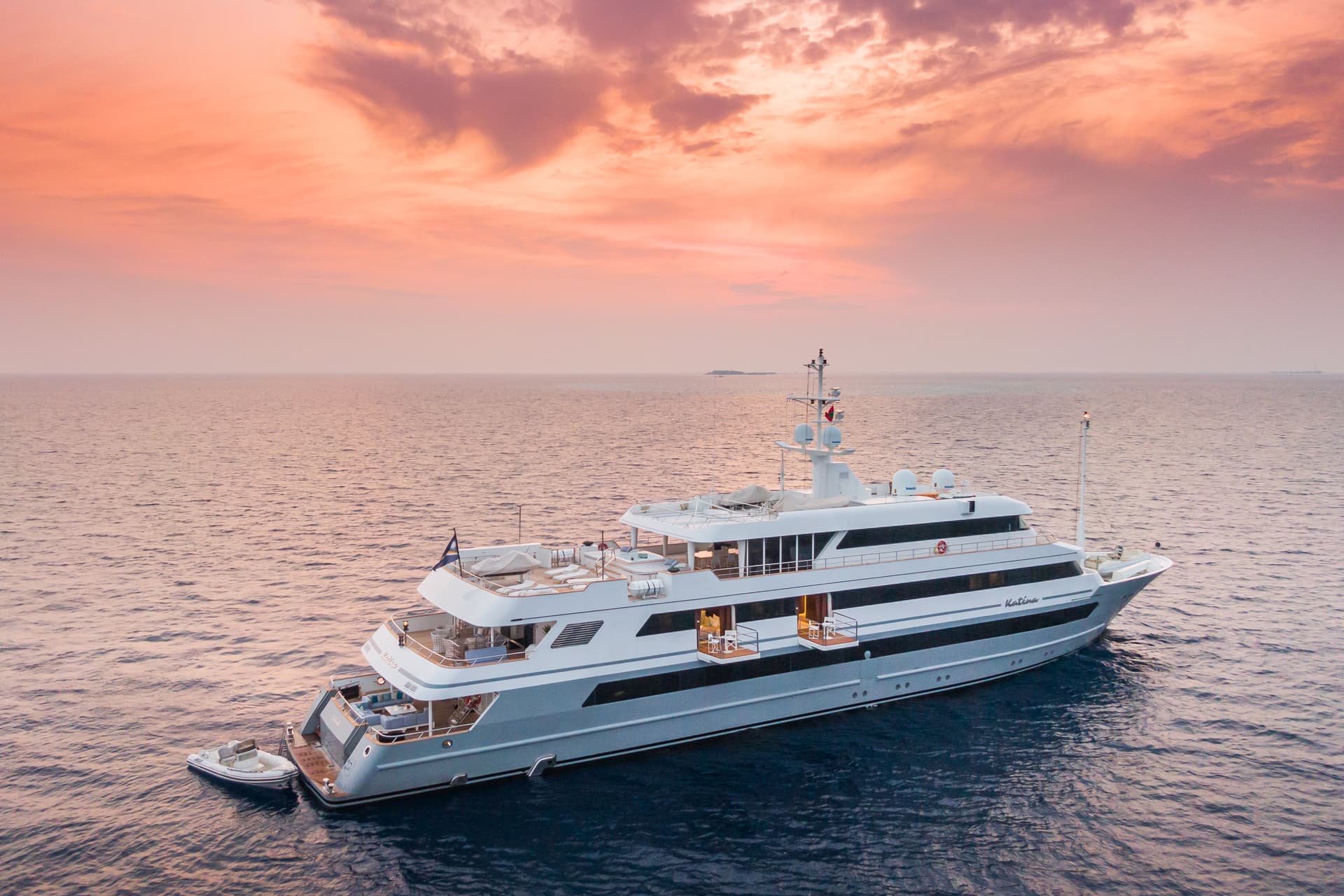 Large yacht anchored on dark water under a dramatic orange and pink sunset sky