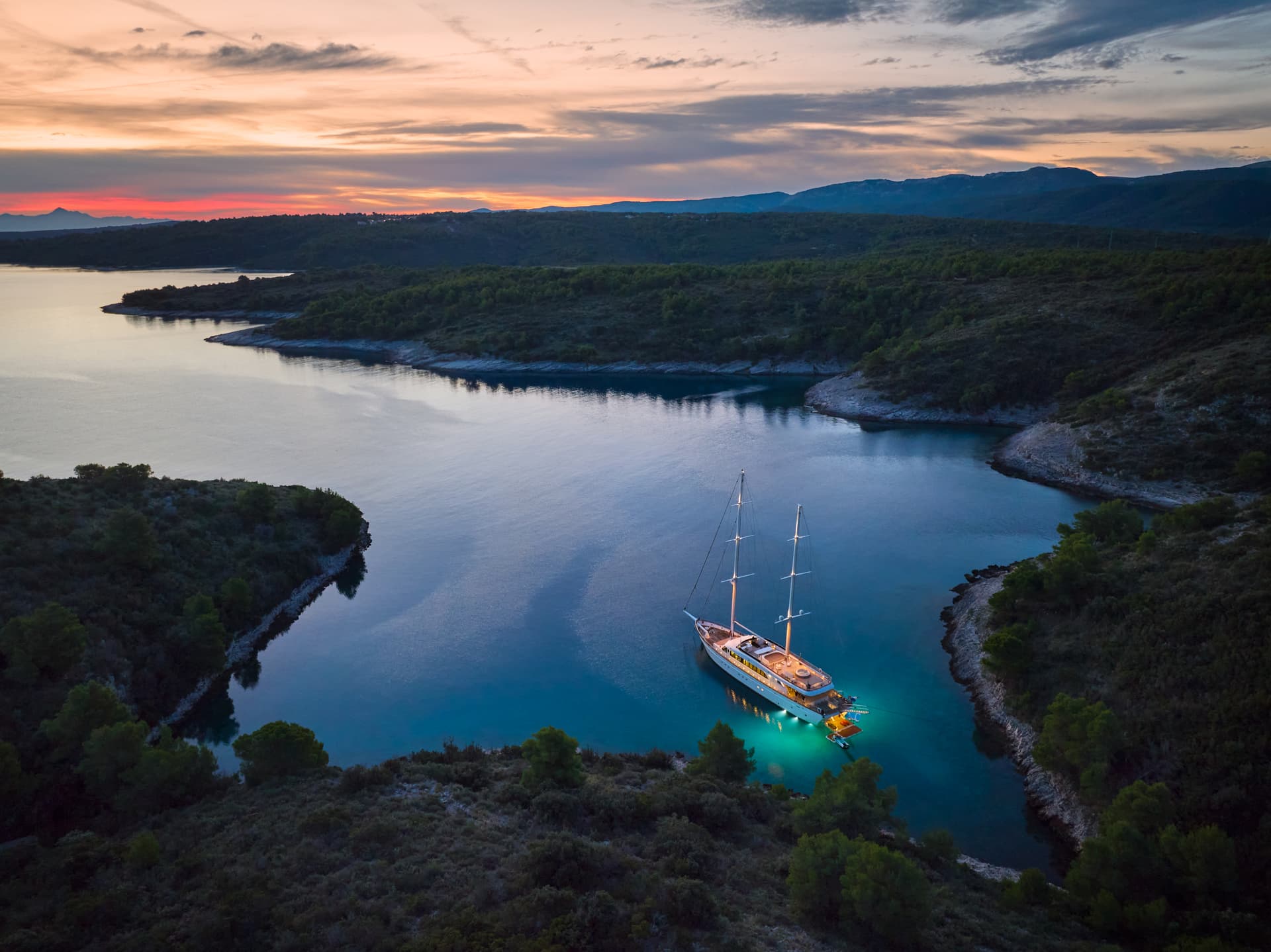 Luxury yacht anchored in a secluded cove with illuminated turquoise water at sunset